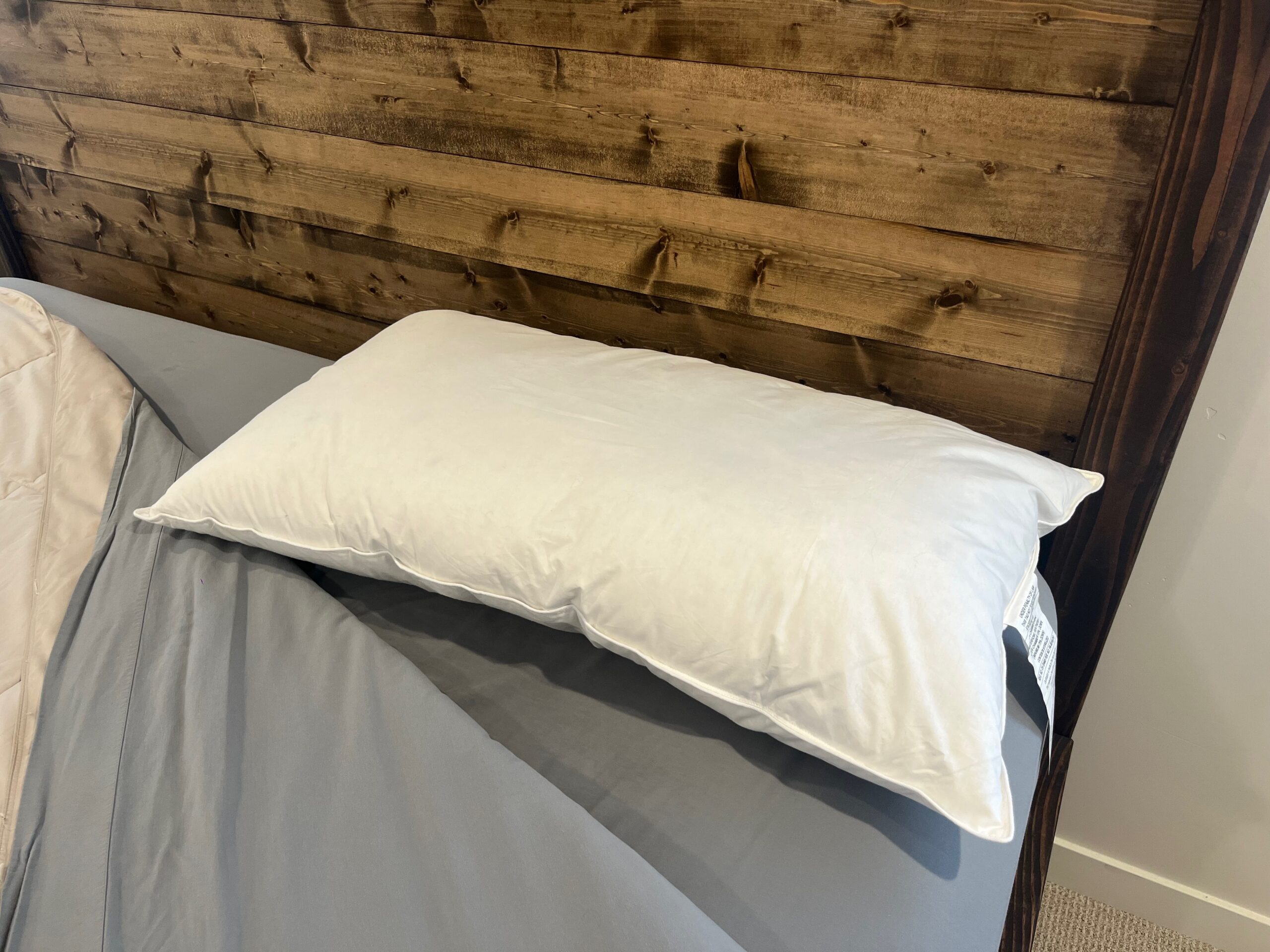 Helix Down Pillow with a white cotton shell, shown flattened on a bed.