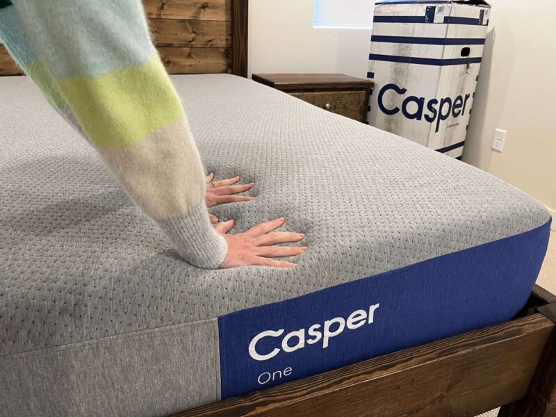 Kristina pressing both hands into the surface of the Casper One mattress to demonstrate firmness.