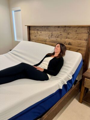 Kristina Hindes reclines on an Amerisleep adjustable bed with the head section raised, smiling while lying on her back with knees bent.