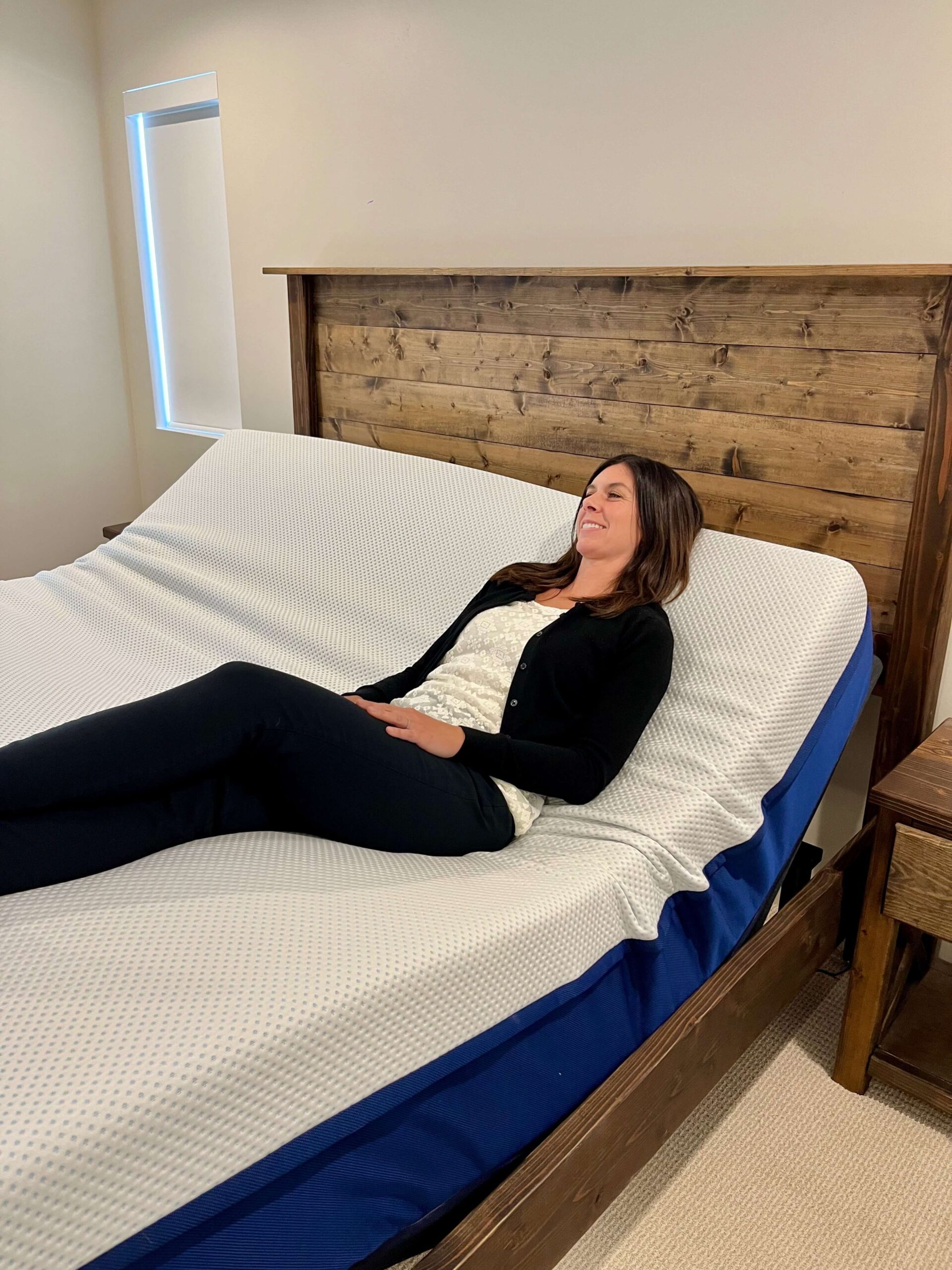 Kristina Hindes reclines on an Amerisleep adjustable bed with the head section raised, smiling while lying on her back with knees bent.