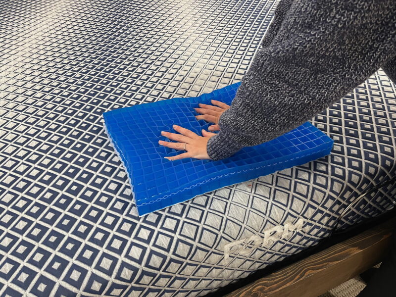 Hands pressing into a blue grid foam layer sample on a FORM Core mattress.