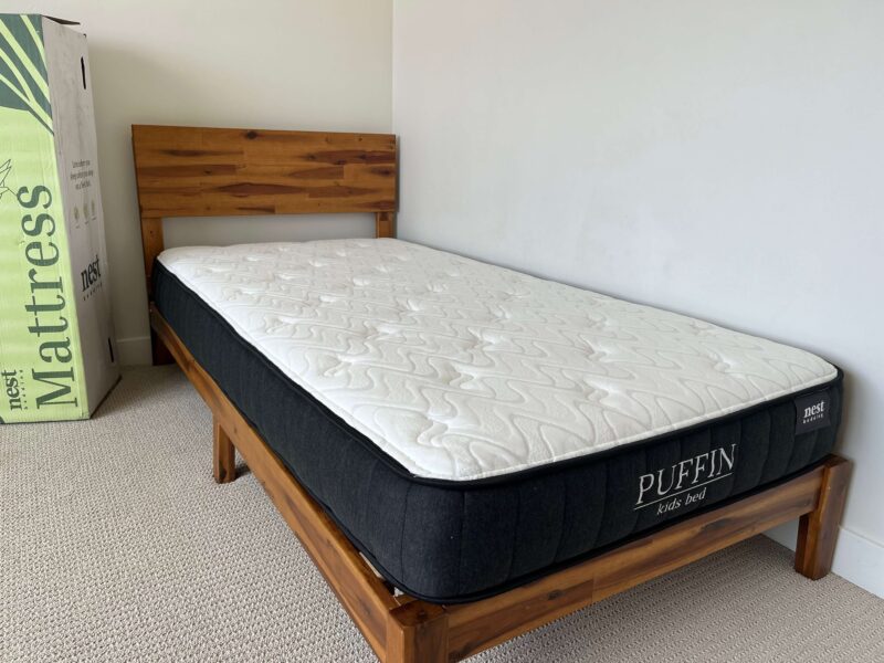 Nest Bedding Puffin kids mattress on a twin wood bed frame with shipping box nearby.