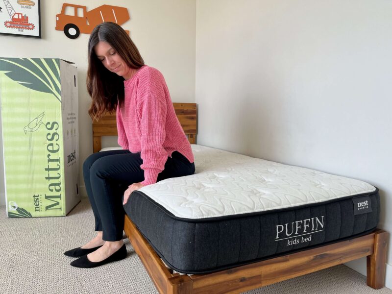 Kristina Hindes sits on the edge of the Nest Bedding Puffin Kids mattress to test edge support.