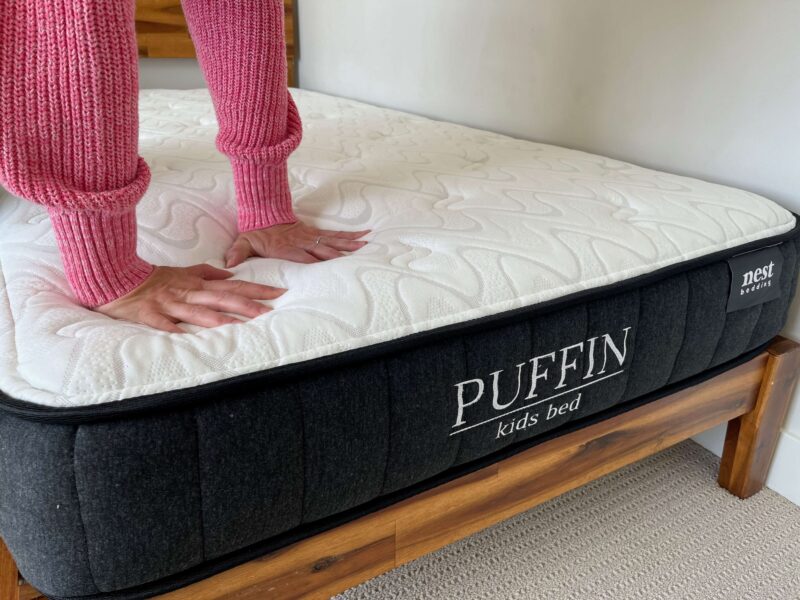 Kristina Hindes presses both hands into the surface of the Nest Bedding Puffin Kids mattress to test its firmness.