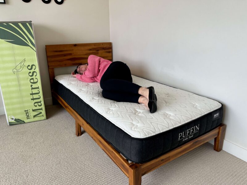 Kristina Hindes lies on her right side on the Nest Bedding Puffin Kids mattress.