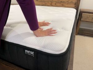 Kristina Hindes presses both hands into the surface of the Nest Bedding Raven mattress to test its firmness.