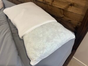 Close-up view of a shredded memory foam pillow with its white geometric-patterned outer cover partially pulled back to reveal the internal fabric liner.