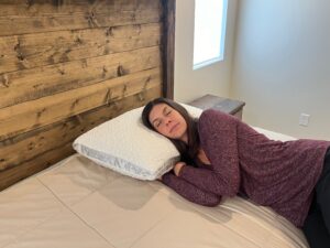 Kristina Hindes rests her head on a Nest Bedding Easy Breather pillow while performing a side-sleeping comfort test on a bed.